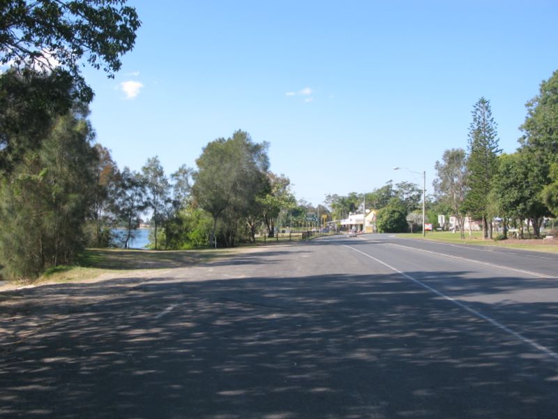 Chinderah Bay Drive - Chinderah: Roadside parking to the left with shops and hotel in the distance.